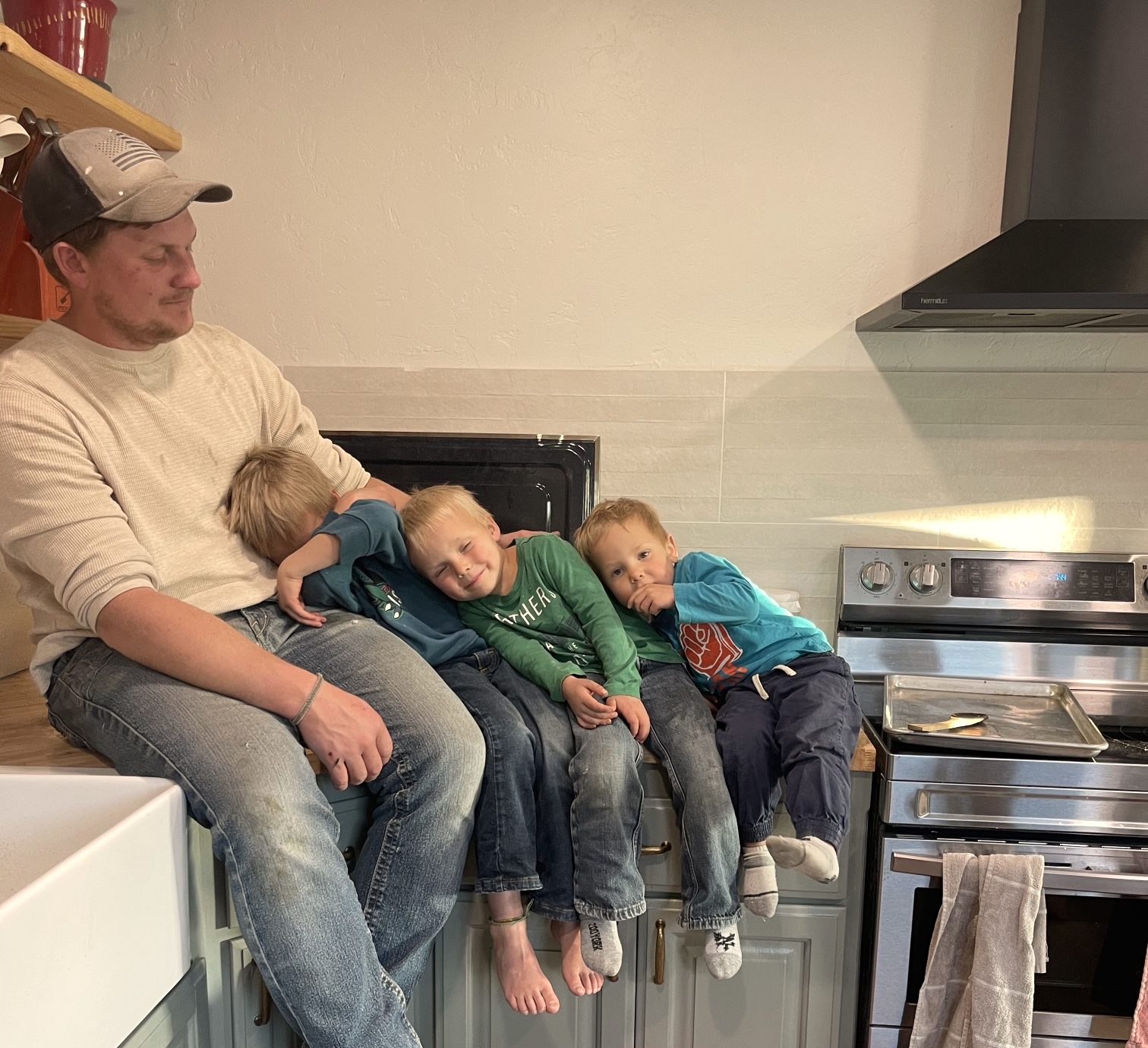 Seth and his three boys sitting on the counter of a sage-green kitchen he built